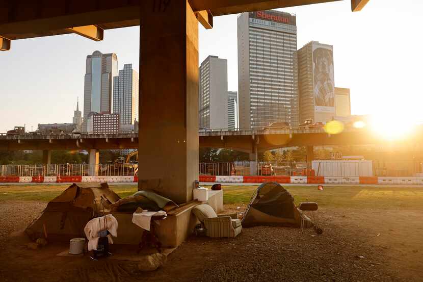The sun sets behind a homeless encampment under the I-345 overhead in downtown Dallas in...