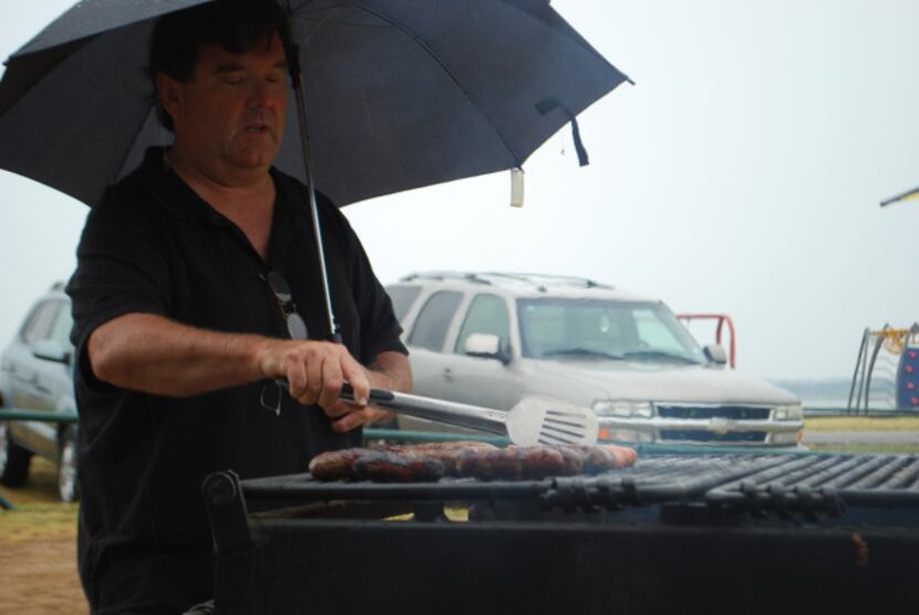 J.D. Ryan cooks bratwursts and hot dogs in the rain Sunday at Meadowmere Park on Grapevine...