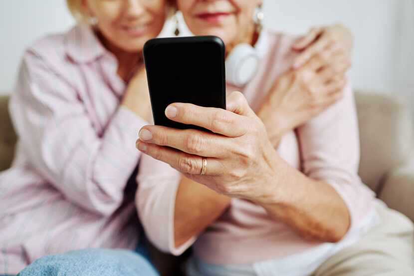 Close up of senior woman holding smartphone with daughter embracing her.