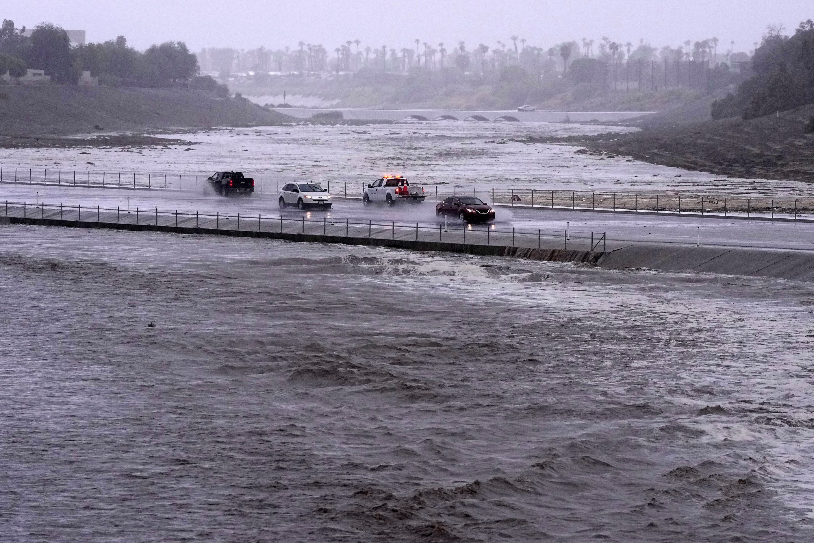 Vehicles cross over a flood control basin that has almost reached the street, Sunday, Aug....