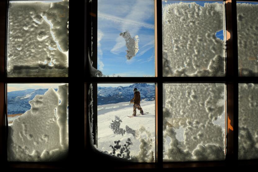 A snowboarder is framed by snow-covered windows on top Panorama Lookout at Mammoth Mountain...