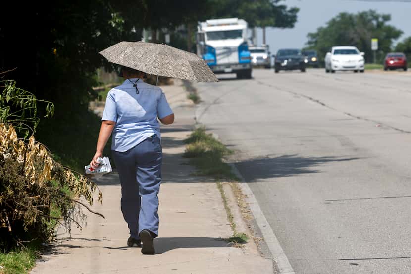 A U.S. Postal Service mail carrier tries to stay cool under the shade of an umbrella as she...