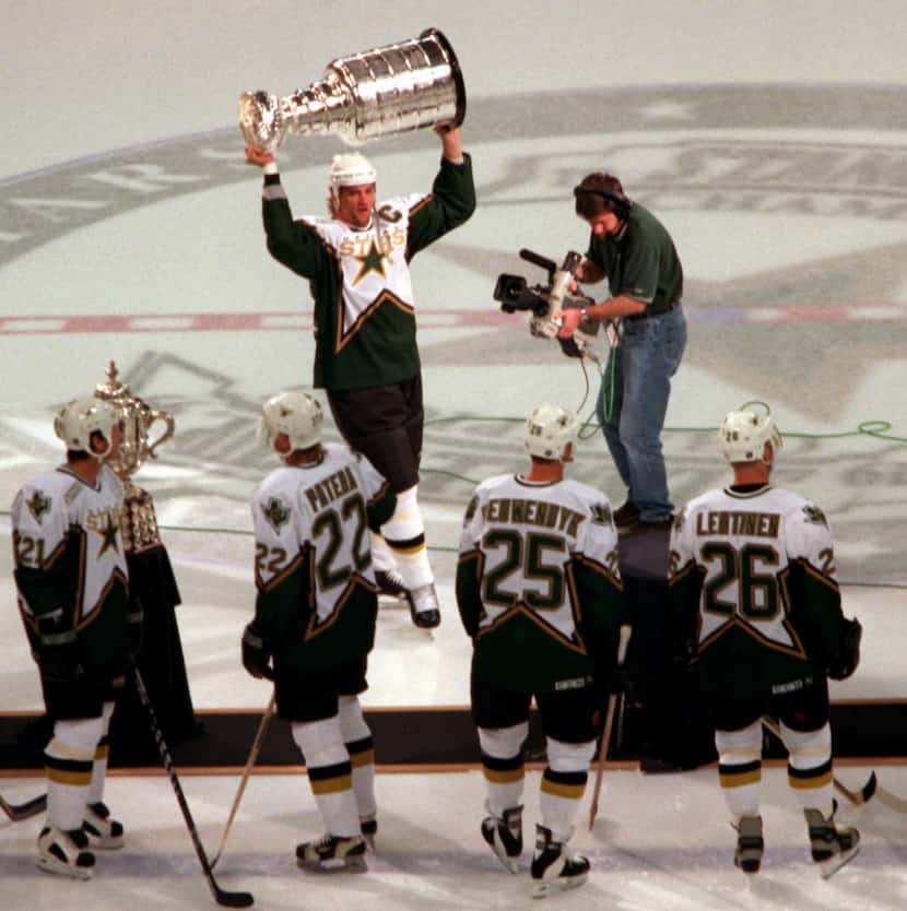 The Dallas Stars captain Derian Hatcher hoists the Stanley Cup as teammates watch before...