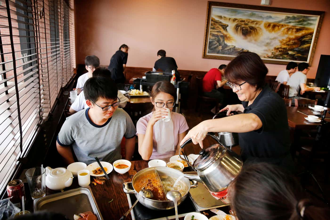 Server Jennifer Ke (right) adds liquid to the hot pot boiling at a table of young diners at...