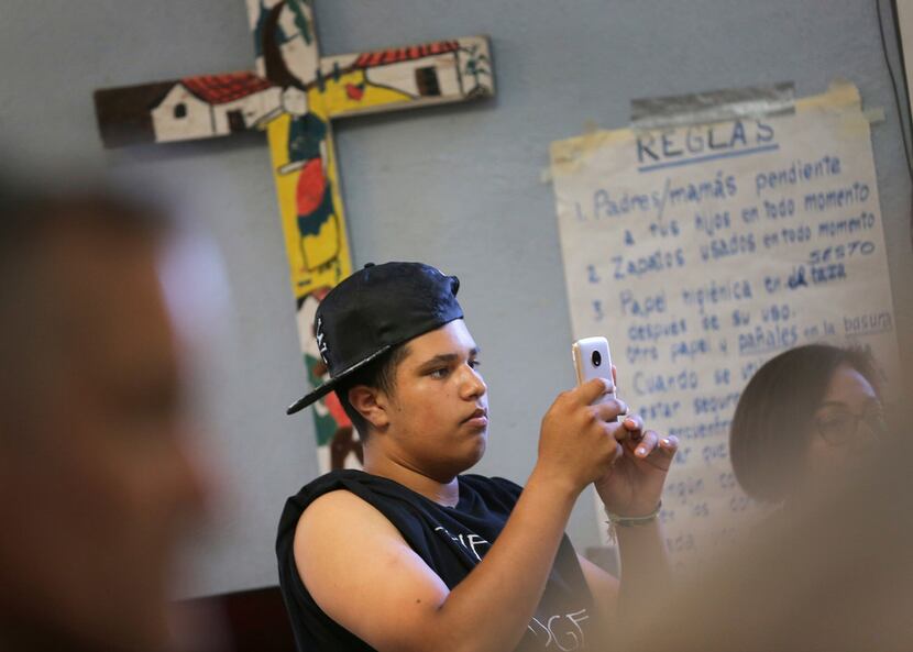 James, 14, takes a picture of his mother, Joselaine, from Brazil, as she speaks at the...