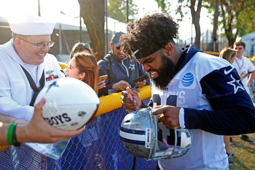 Dallas Cowboys running back Ezekiel Elliott, right, signs autographs for Christopher Smith...
