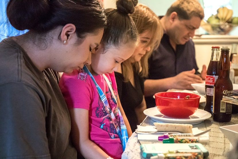 The family members bow their heads in prayer during a meal in Richardson.