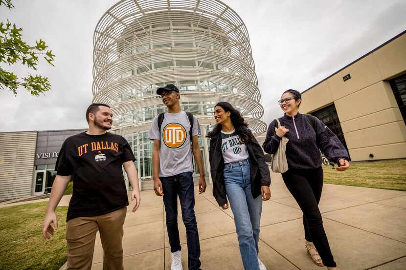 Four college students walk together on the UT Dallas campus, wearing t-shirts with the...