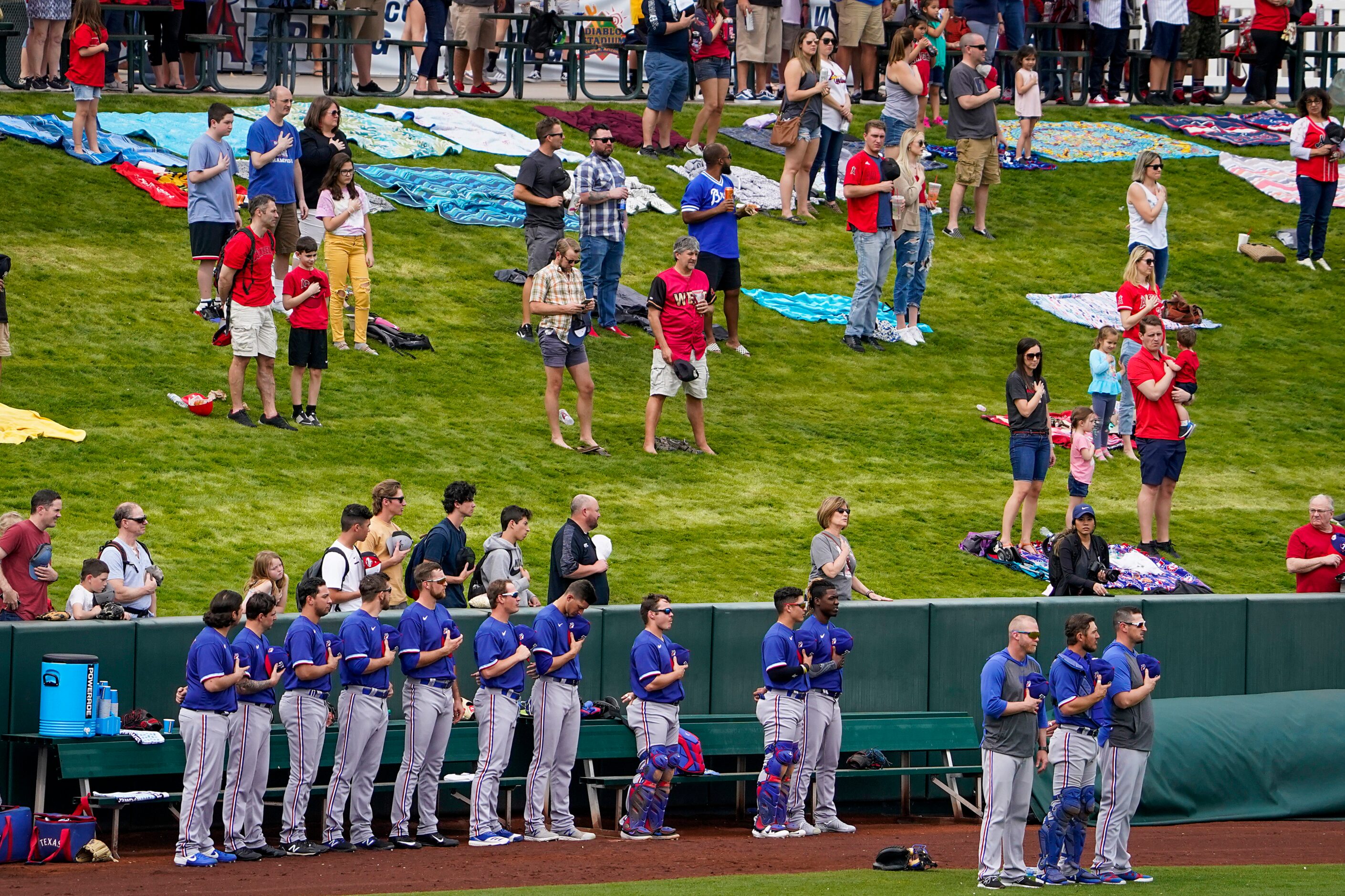 Fans stand along with the Texas Rangers bullpen for the national anthem before a spring...