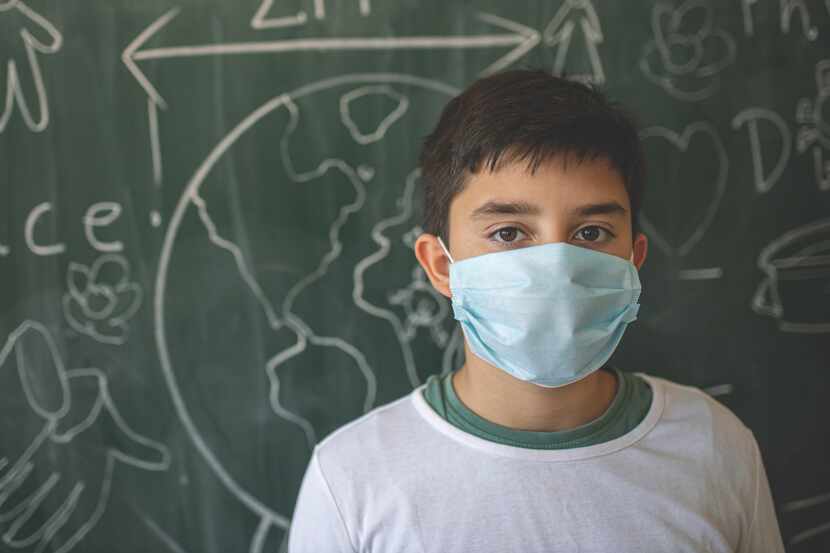 Portrait of a school boy with a face mask in front of the blackboard with social distance signs
