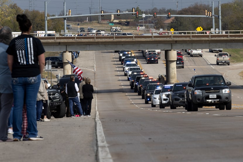 A crowd watches the procession honoring police officer Cooper Dawson, who was fatally shot...