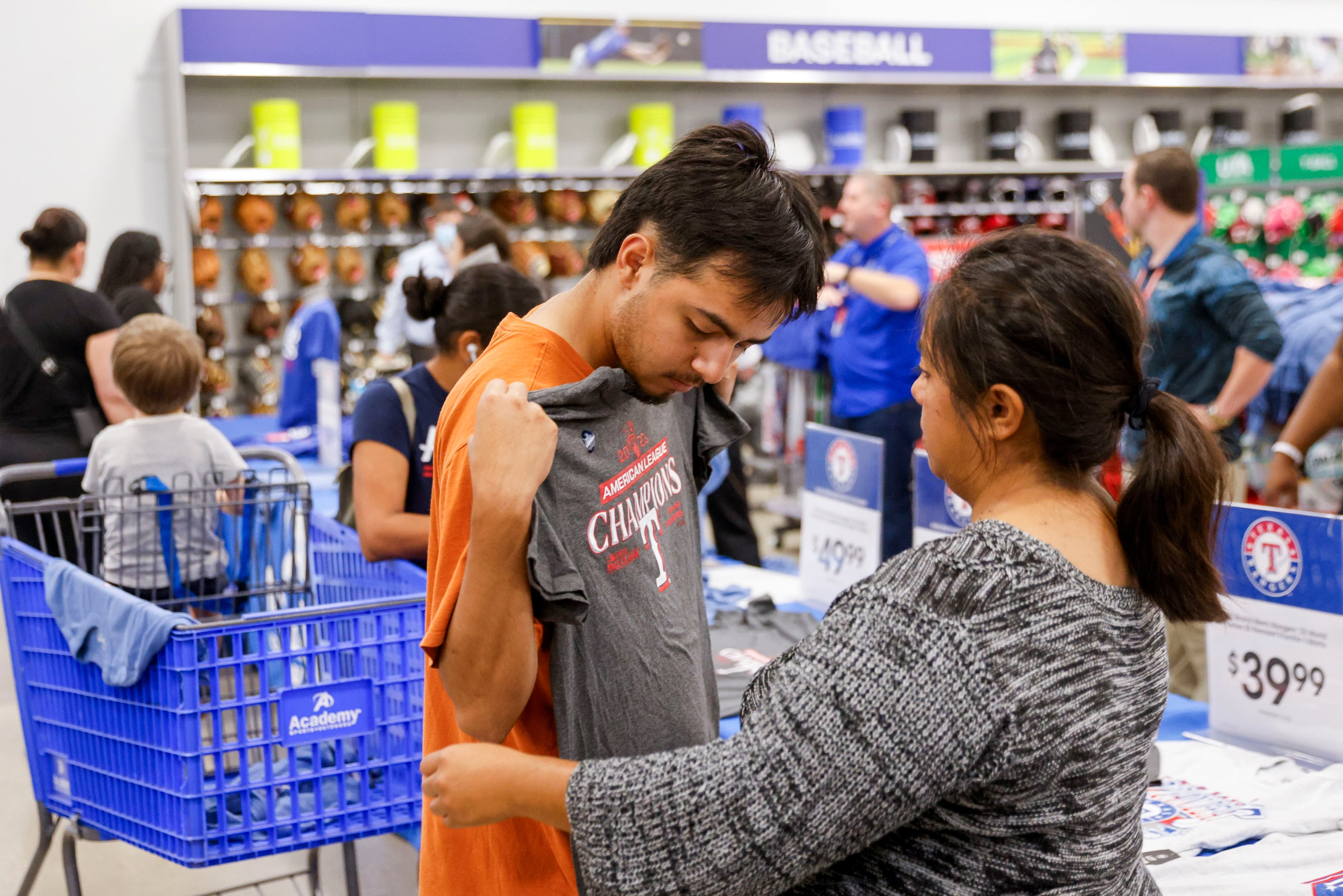 Aaron Lara (left) of Dallas shows a Texas Rangers Champion theme shirt to Alma Lara as they...