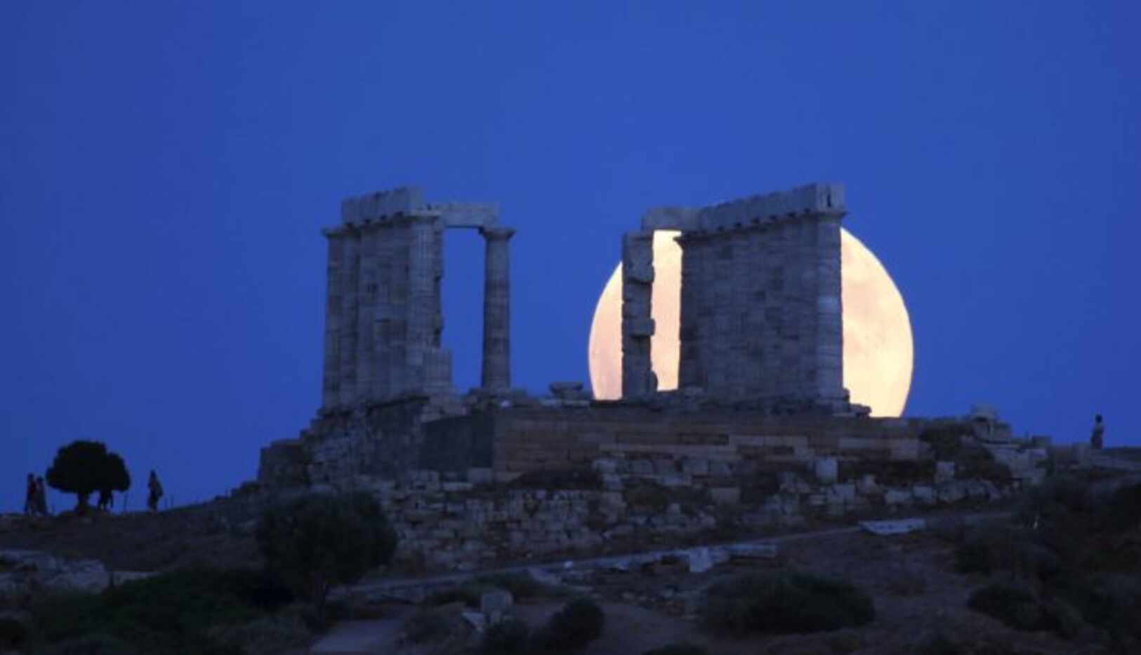 
				La Luna llena se levanta detrás del antiguo templo de Poseidon en cabo de Sunión, a...