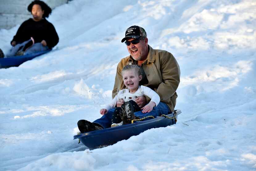 Rodney Allison and his granddaughter ride down a snow hill during Six Flags Over Texas'...
