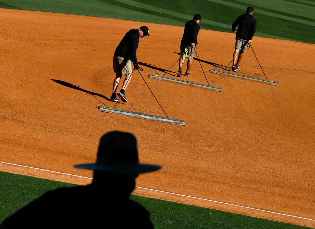 Groundsmen work on the field between innings during a spring training game between the Texas...