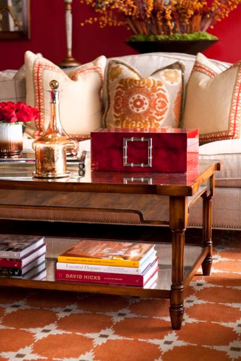 
A cocktail table topped with a red lacquer box, glass decanter and mercury glass candle...