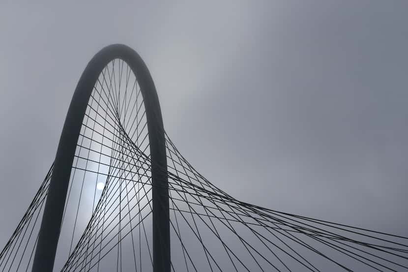 The sun shines through the clouds behind the Margaret Hunt Hill Bridge on a foggy morning on...