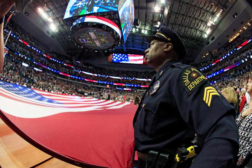 A member of the Dallas Police Department holds an American flag during the national anthem...