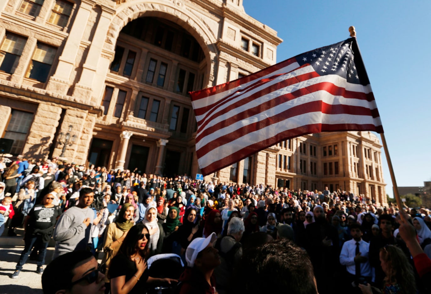 People gather as the national anthem is sung during a press conference at the steps of the...