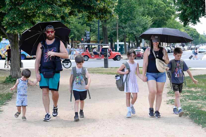 Jordan Savant, second from left, walks with his family carrying umbrellas on the National...
