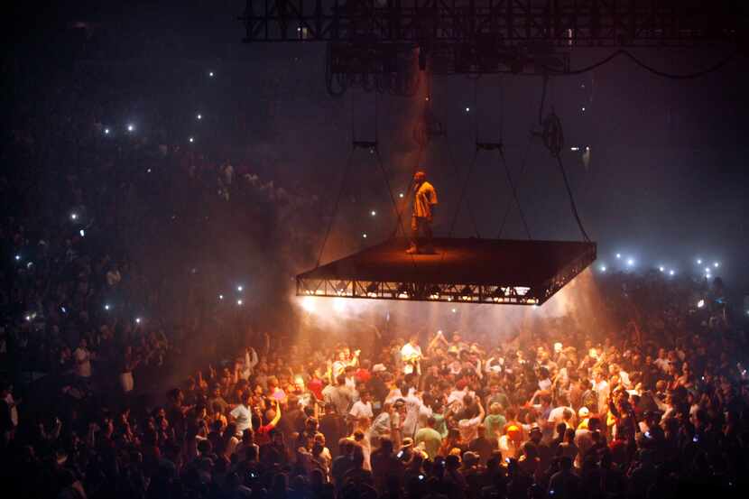American recording artist Kanye West stands on a stage that hovers over the crowd during his...
