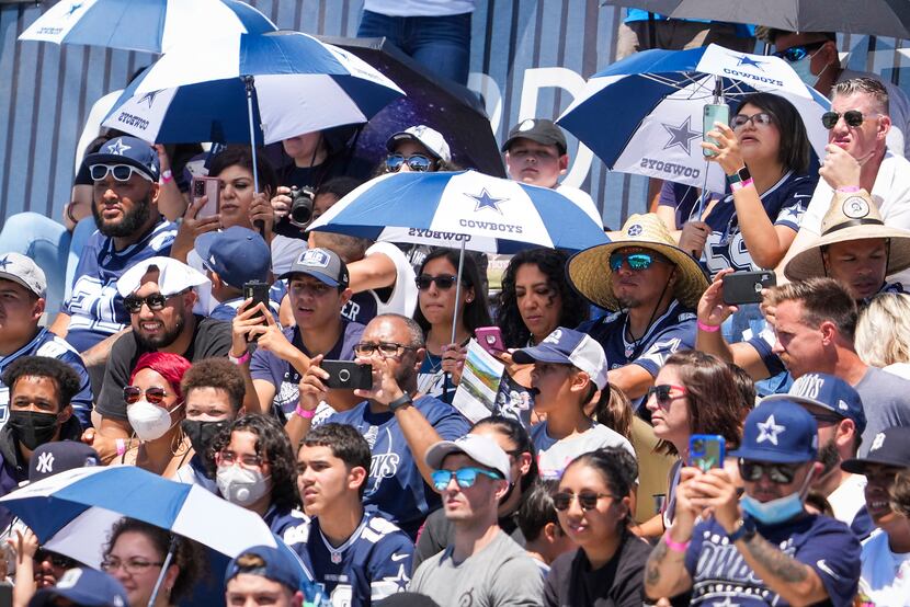 Dallas Cowboys fans use umbrellas for shade as they watch a practice at training camp on...