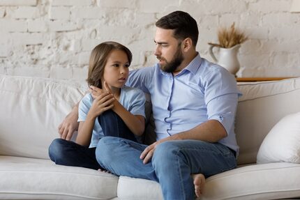 Father and son have a conversation on their couch at home.