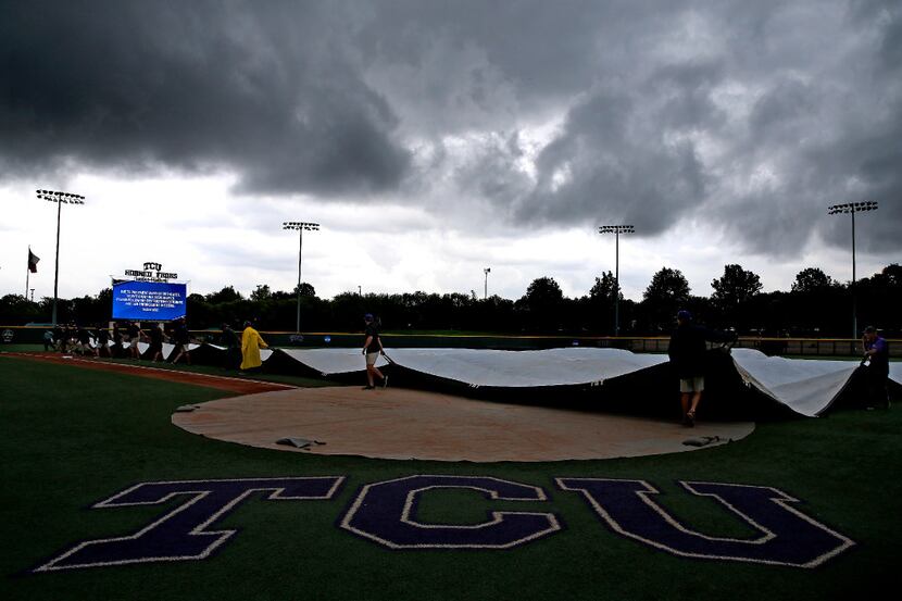 Members of the TCU grounds crew cover the infield with a tarp due to a weather delay during...