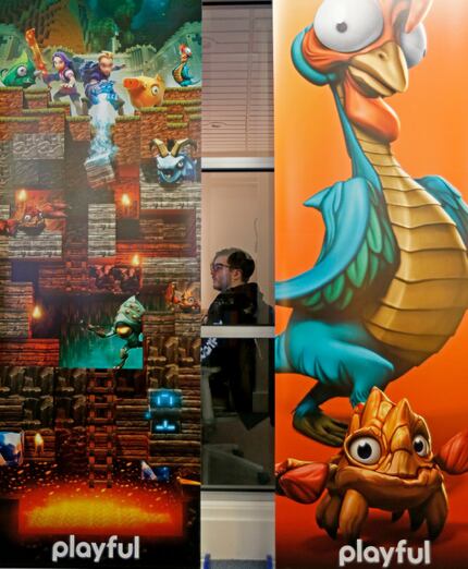 Technical artist Tim Curry works at his desk behind two game banners at Playful Corp.