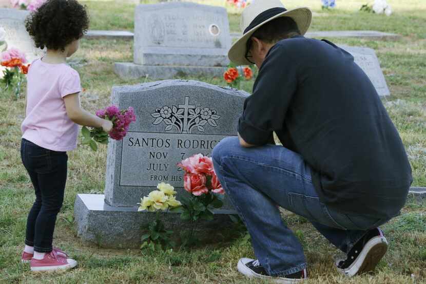 Roberto Corona and his daughter, Sophia, 2, place flowers at Oakland Cemetery on Friday,...