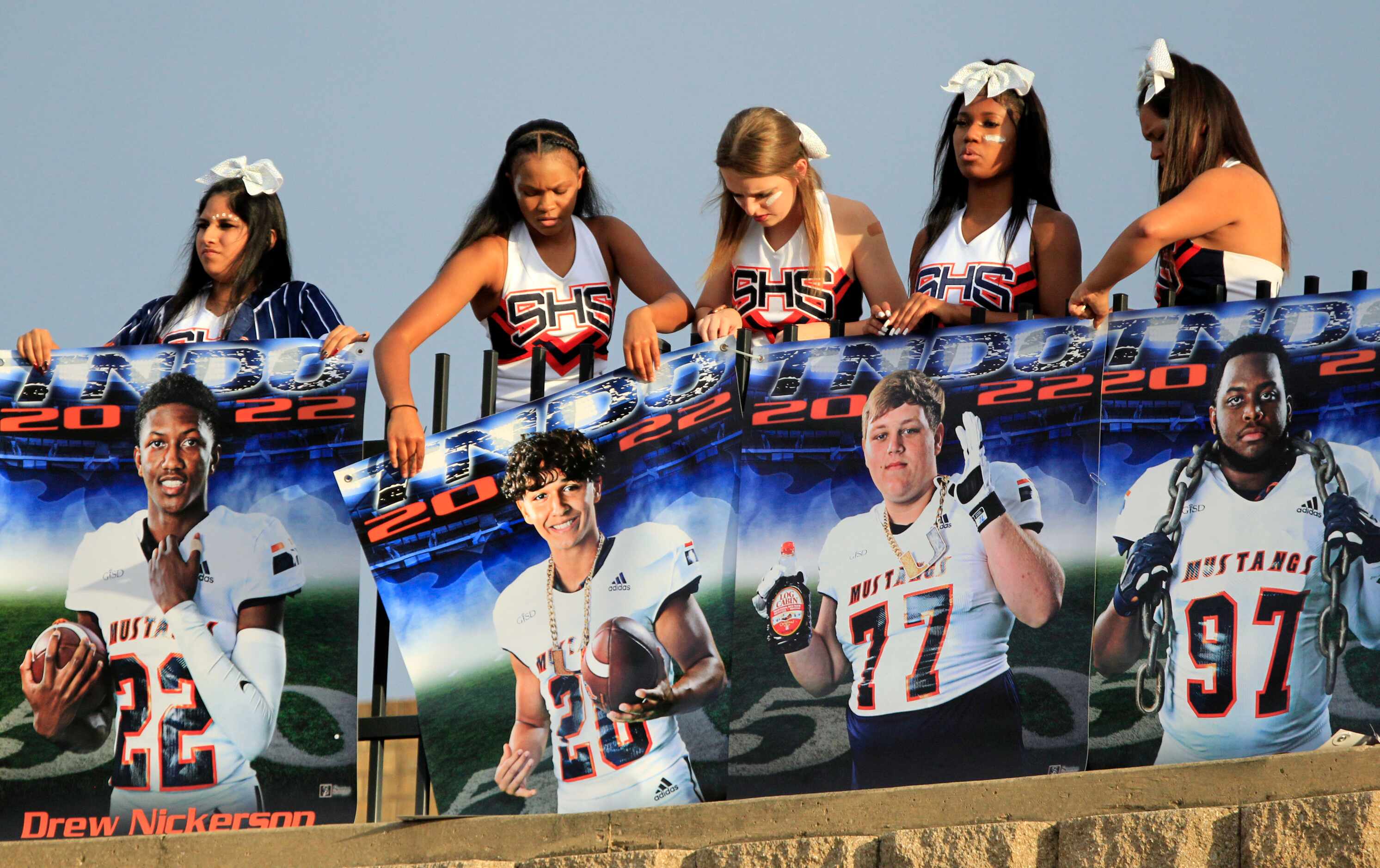 Sachse cheerleaders hang player’s photos on a railing before the start of a high school...