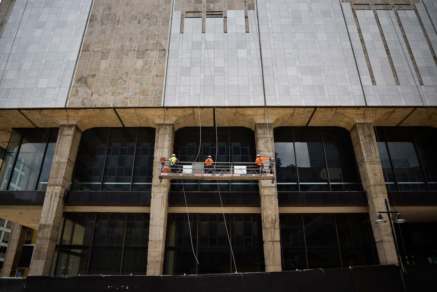 Construction workers use a scaffold to be lifted high above the ground to install marble on...