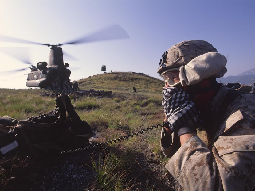 A U.S. Marine speaks into a radio on a mountaintop after an insert of troops by a CH-47D...