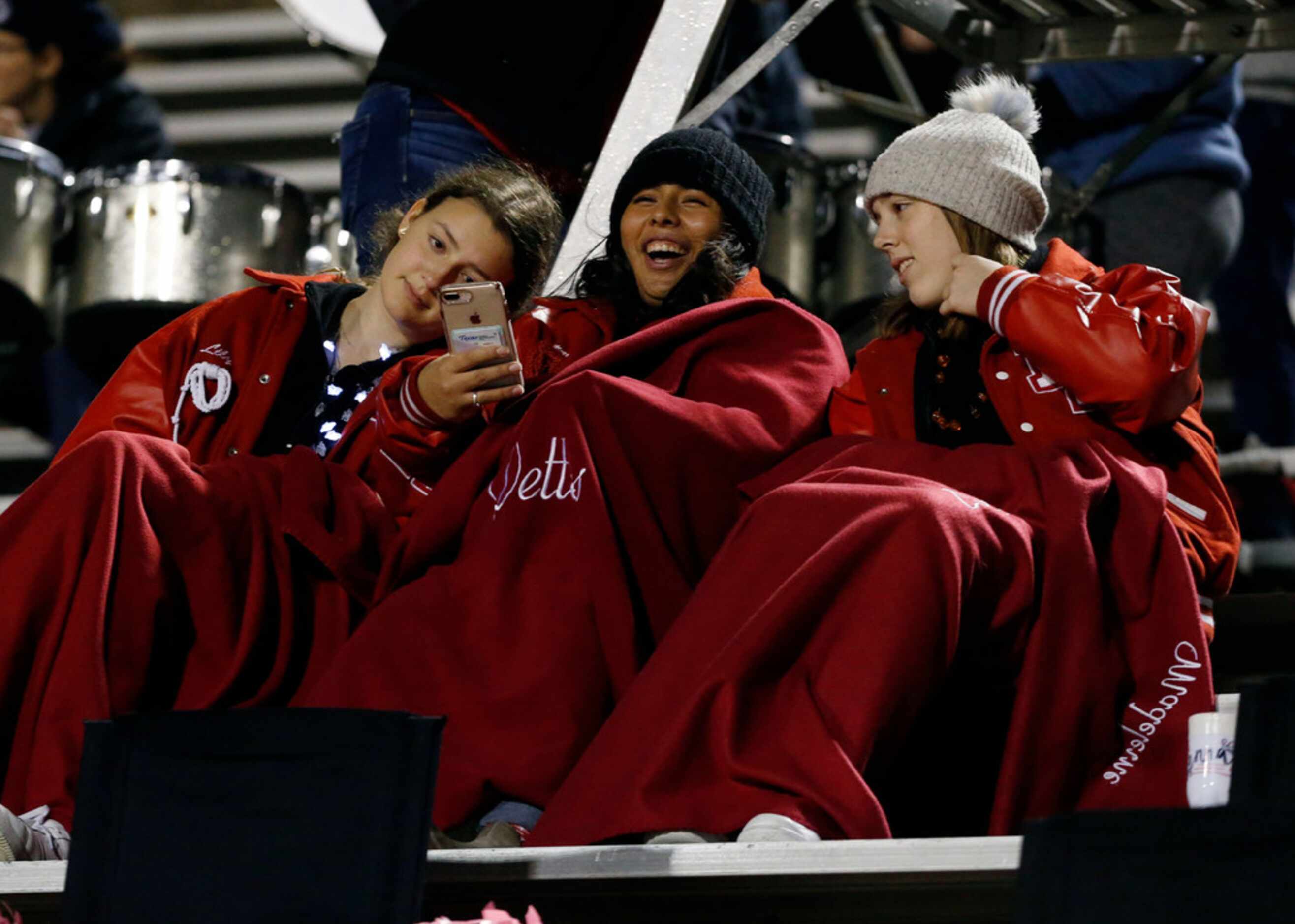 Three bundled up Lake Highlands students enjoy looking at a mobile phone during the first...