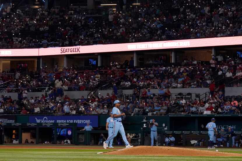 The lights dim and fans turn on lights on their smart devices as Texas Rangers relief...