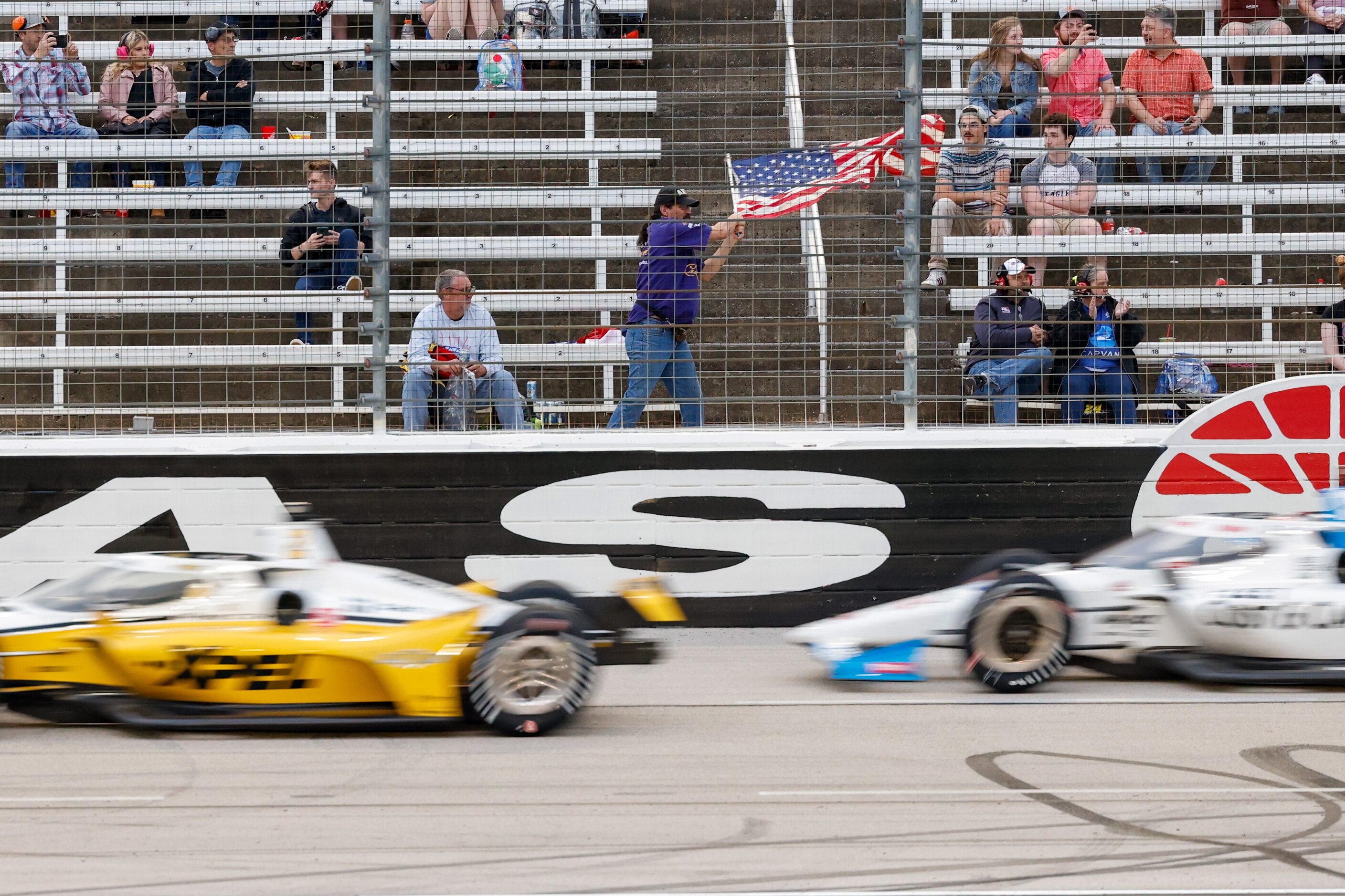 A fan waves an American flag as drivers race by during the IndyCar Genesys 300 at Texas...