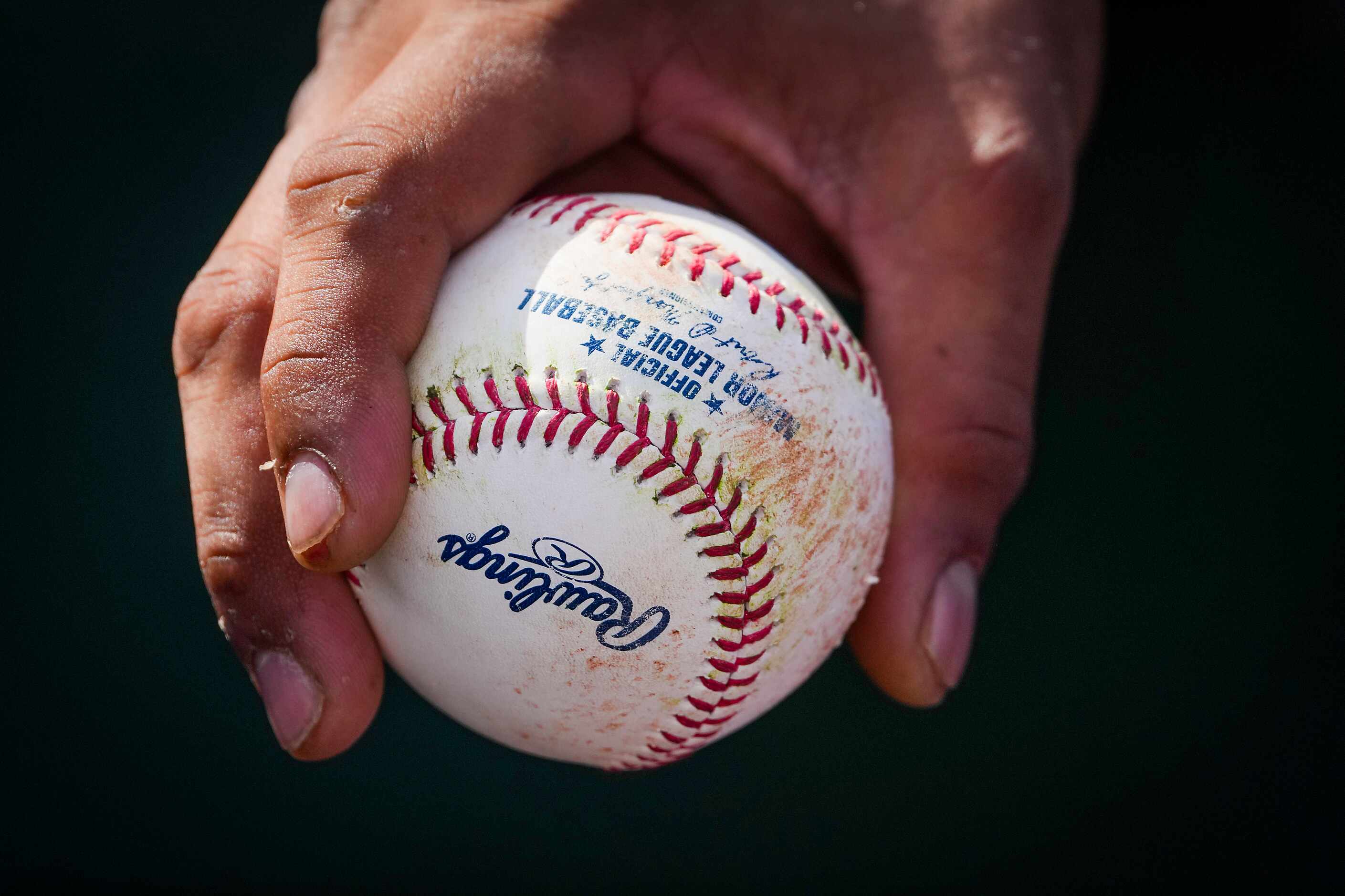 A Texas Rangers player holds a ball in the dugout during a spring training game against the...