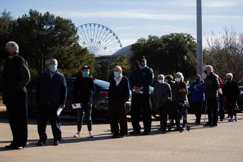 People wait in line for a golf cart in the parking lot of Fair Park before they receive the...