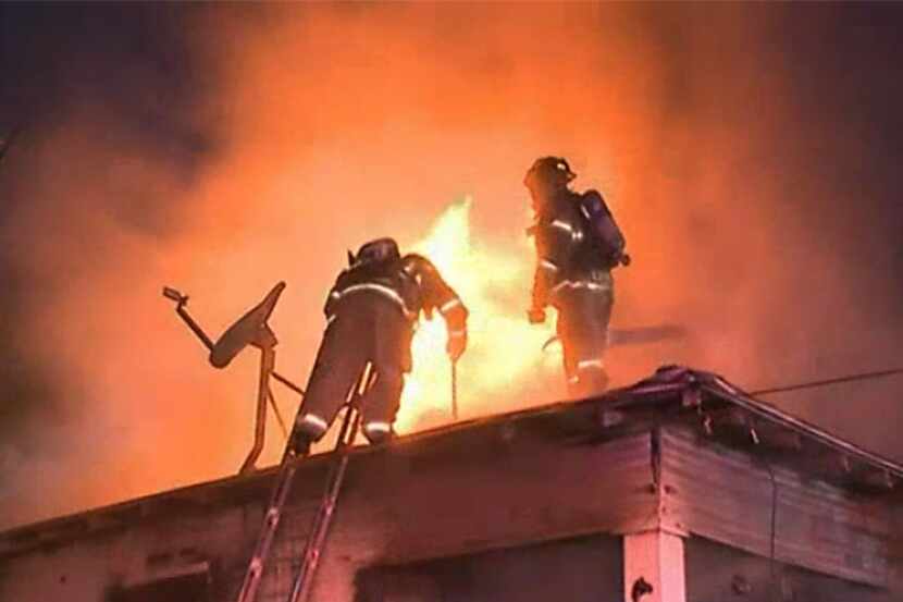 Dallas firefighters stand on the roof while fighting a house fire early Wednesday morning in...