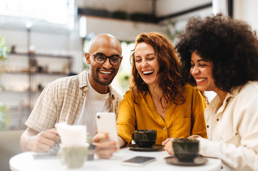 Friends enjoy making a video call in a coffee shop, connecting with their other friends as...