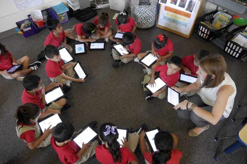 Momentous School of Dallas students form a circle as they do work on tablets.