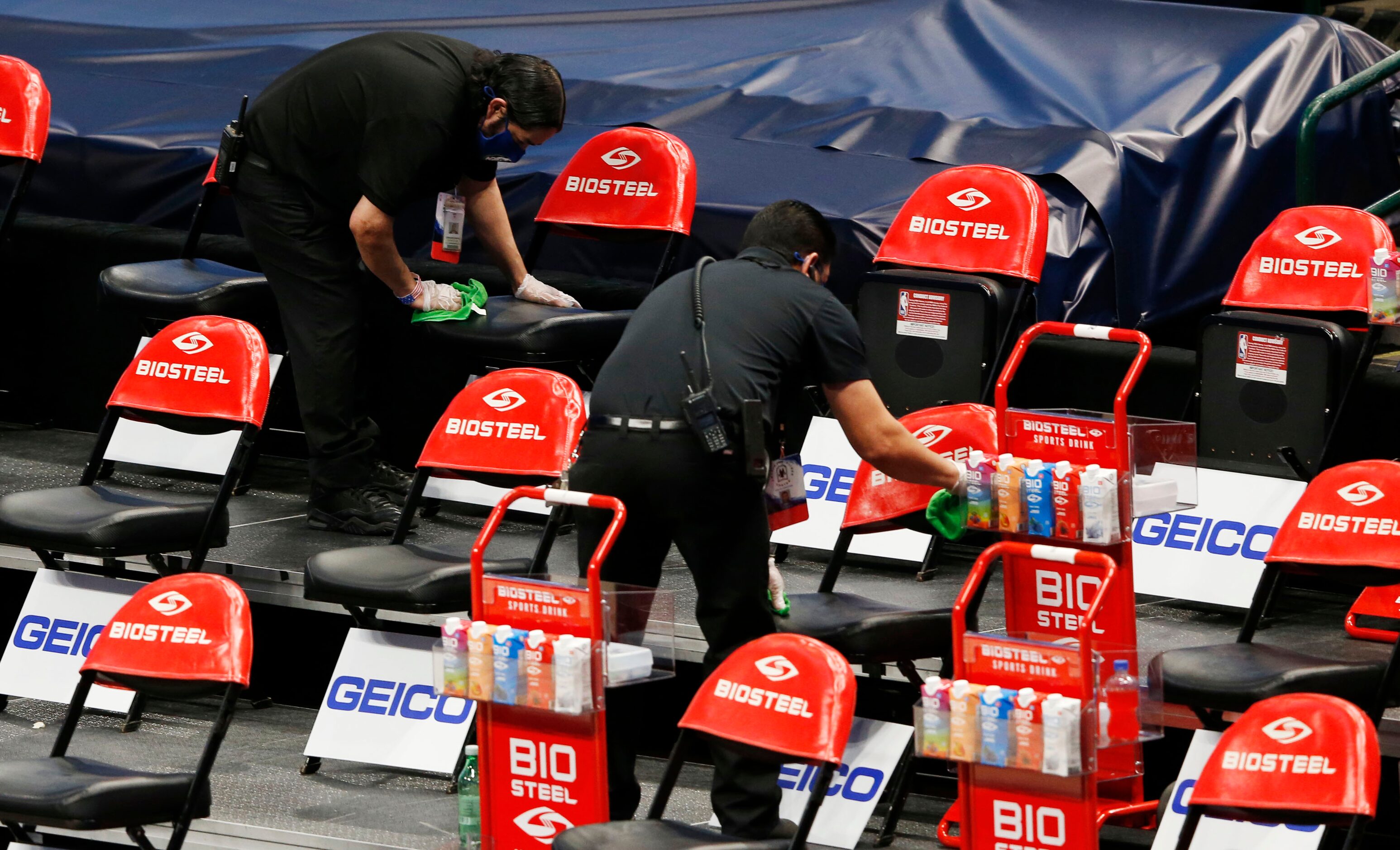 Employees clean the seats where players and coaches sit before a game between the Dallas...