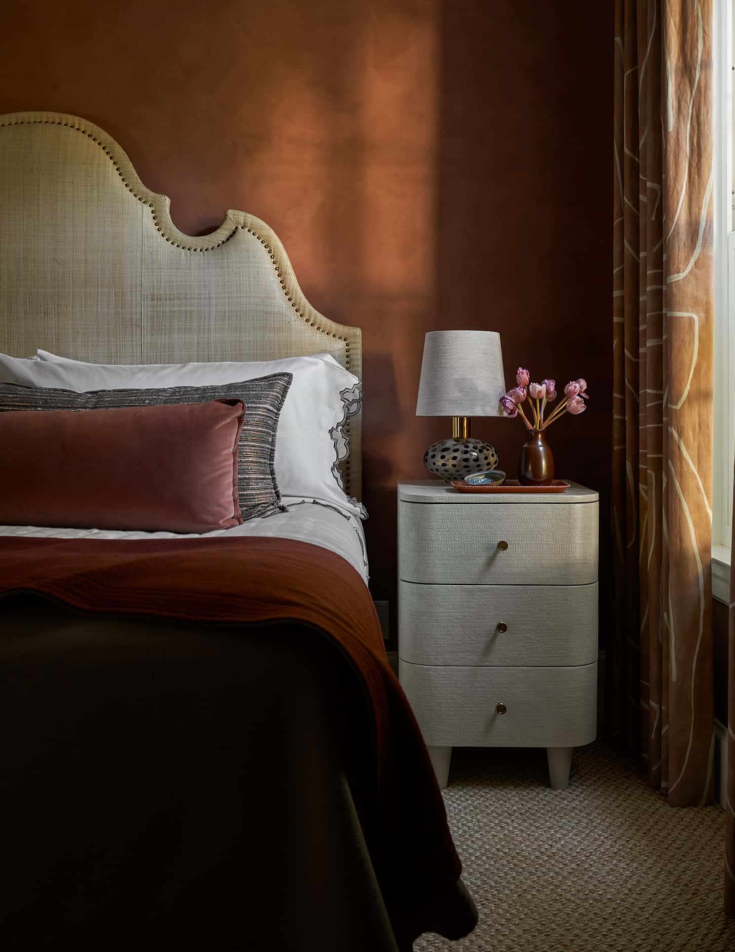 Bedroom with rusty orange walls, orange curtains and deep orange-red bedding with a detailed...