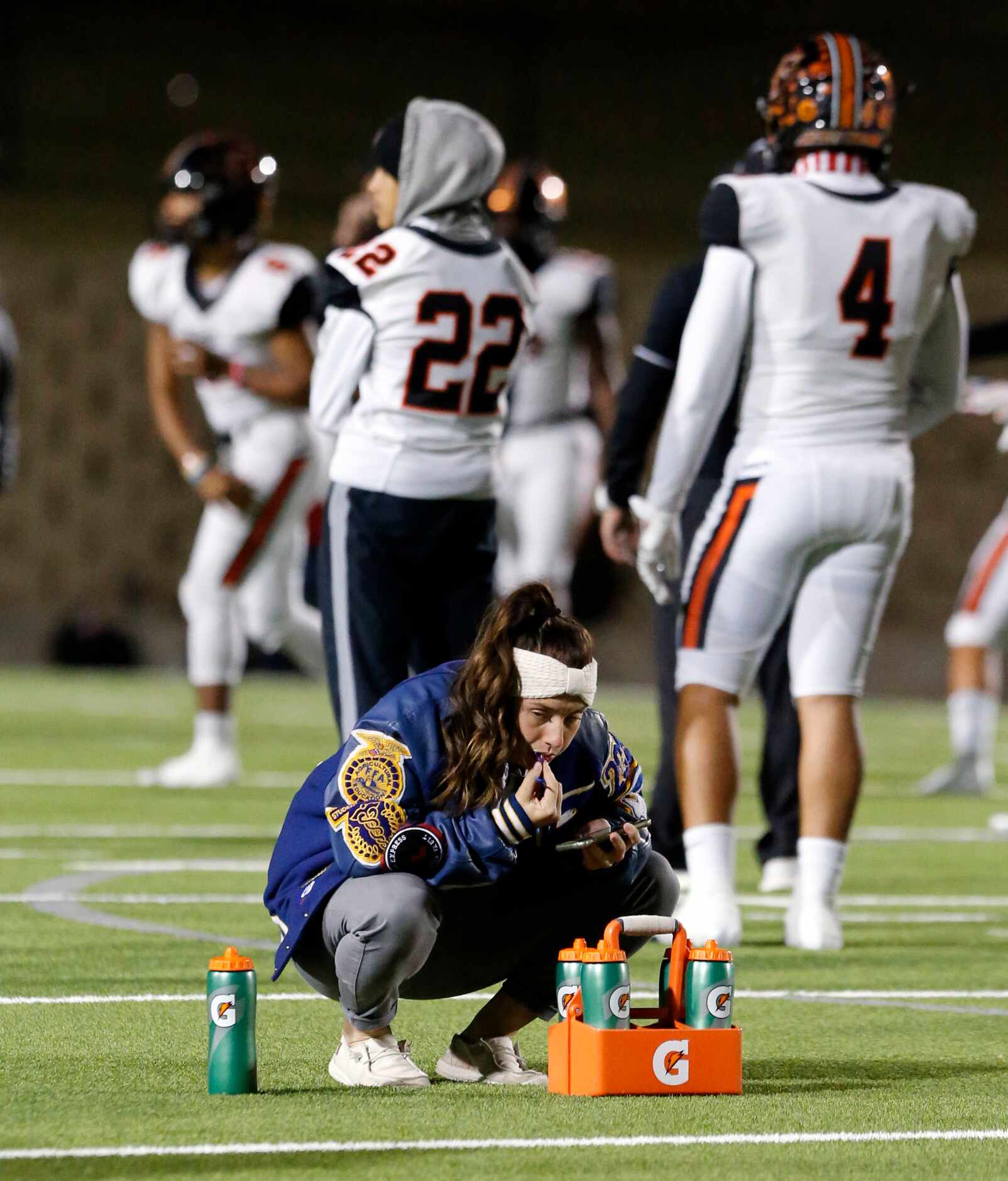 A Farris High trainer checks her phone on the field during pregame workout before the start...