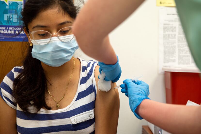 A Dallas County nurse vaccinates 14-year-old Montcerrat Sandate with her second dose of the...