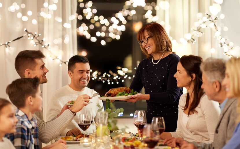 Happy woman offering roast chicken to family having dinner party at home.