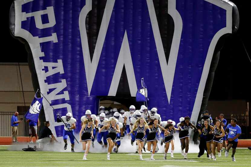 The Plano West team and cheerleaders run onto the field through the team's giant blowup...