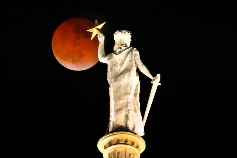 The full Super Flower Blood Moon eclipse rises over the Goddess of Liberty atop the Texas...