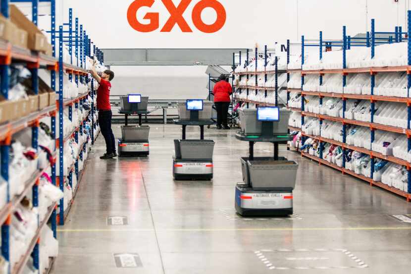 Workers pick products off shelves accompanied by robots at a GXO Logistics site.