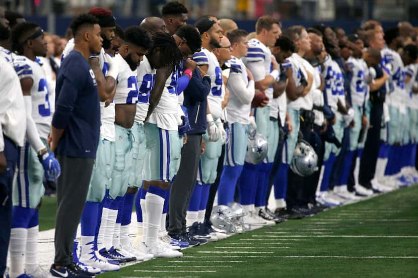 The Dallas Cowboys and staff stand on the sideline during the playing of the national anthem...